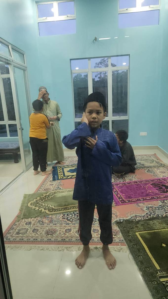 Seorang kanak-kanak berdiri di atas sejadah sedang menunaikan solat